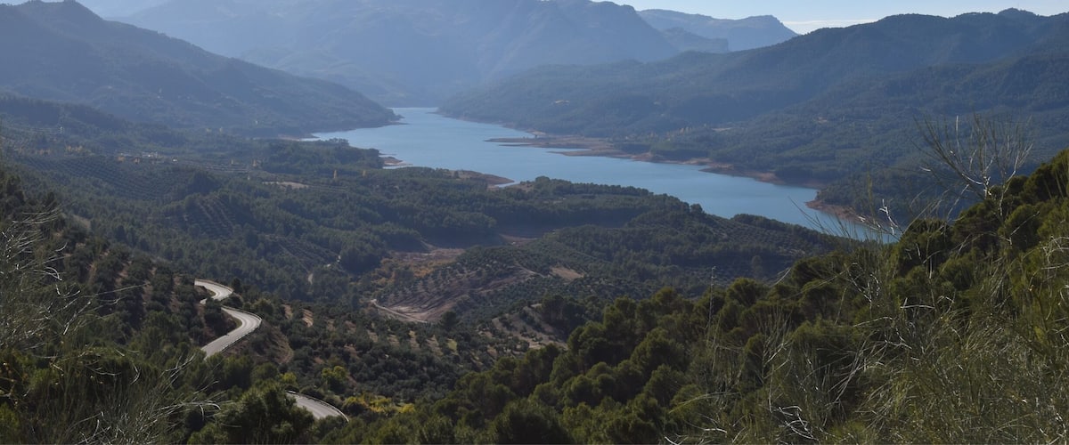 A winding road through a mountainous landscape with a lake in the valley.