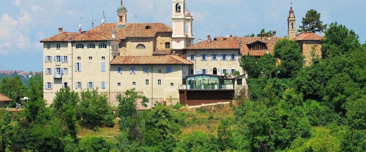 A historic building with multiple towers and a clock, surrounded by lush greenery.