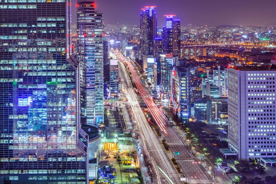 A nighttime cityscape with illuminated skyscrapers and a busy highway.