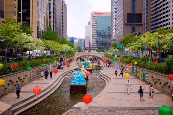 A city square with a water feature, surrounded by modern buildings and decorated with colorful lanterns.
