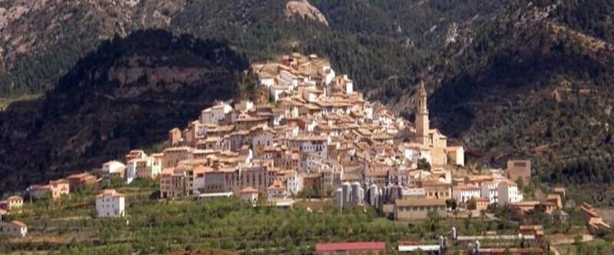 A town nestled in a valley with a prominent church spire, surrounded by mountains.