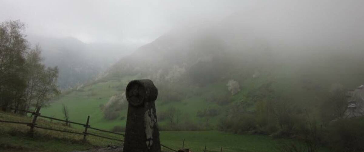 A foggy landscape with a stone monument in the foreground and rolling hills in the background.