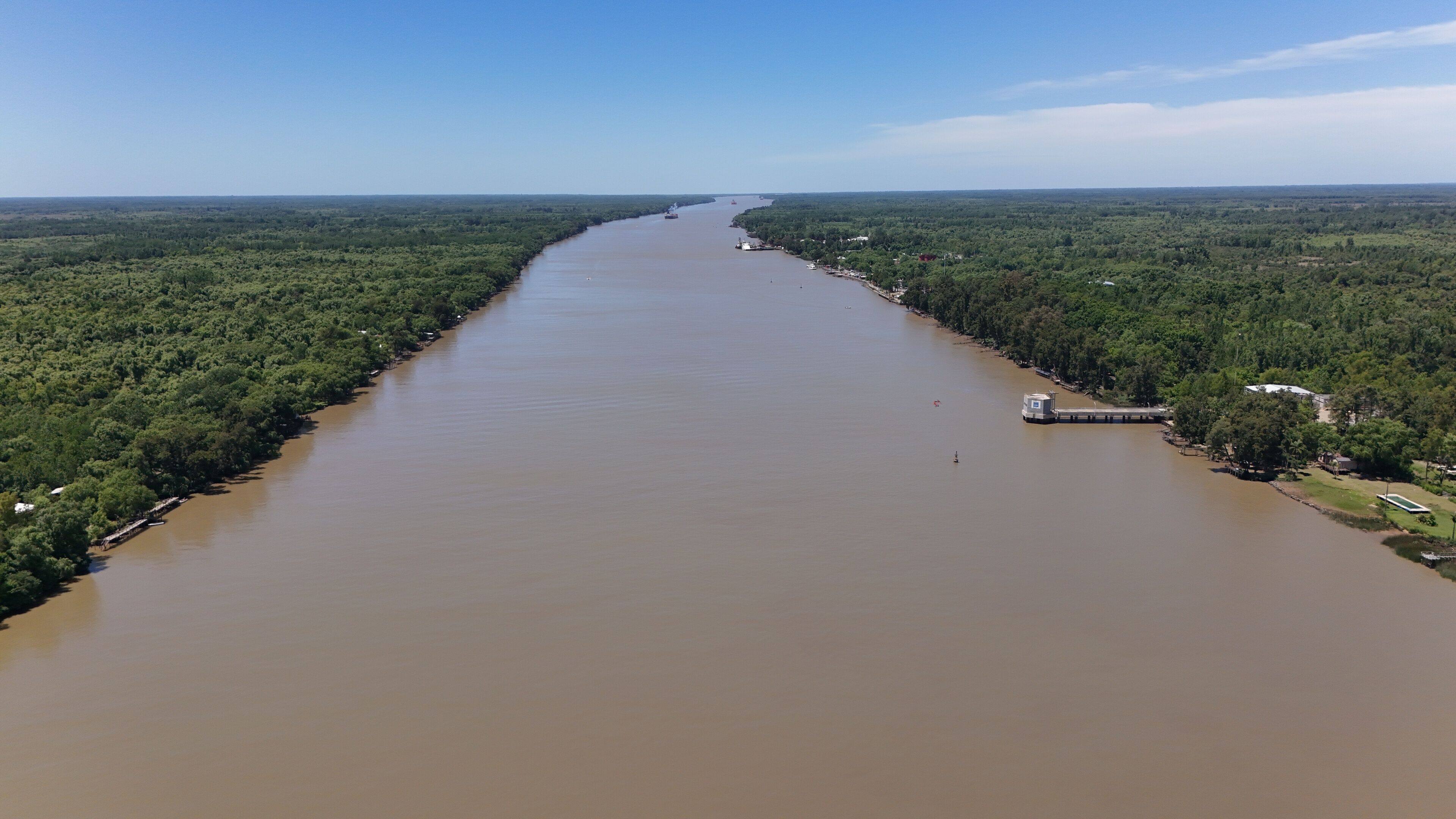 A wide river flanked by dense forests, with a small dock and a boat visible on the right bank.