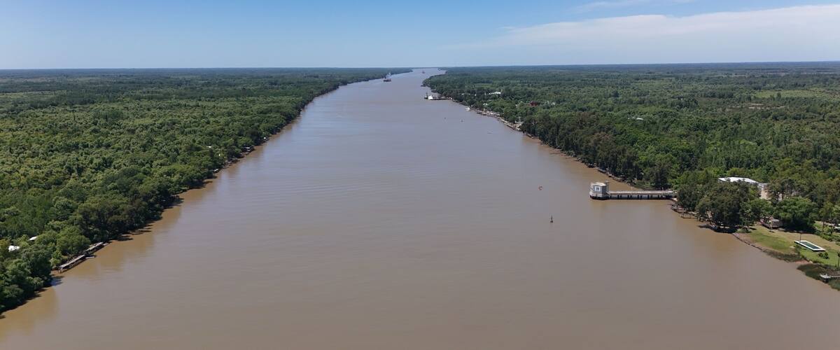 A wide river flanked by dense forests, with a small dock and a boat visible on the right bank.