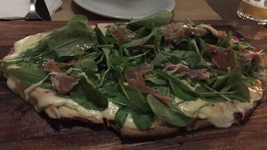 A pizza with spinach and prosciutto on a wooden board.