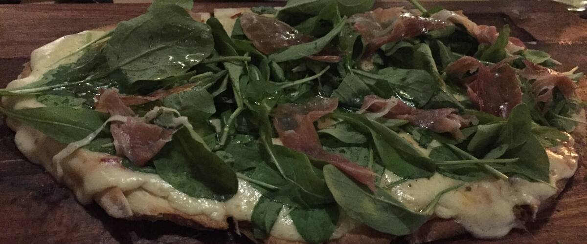 A pizza with spinach and prosciutto on a wooden board.