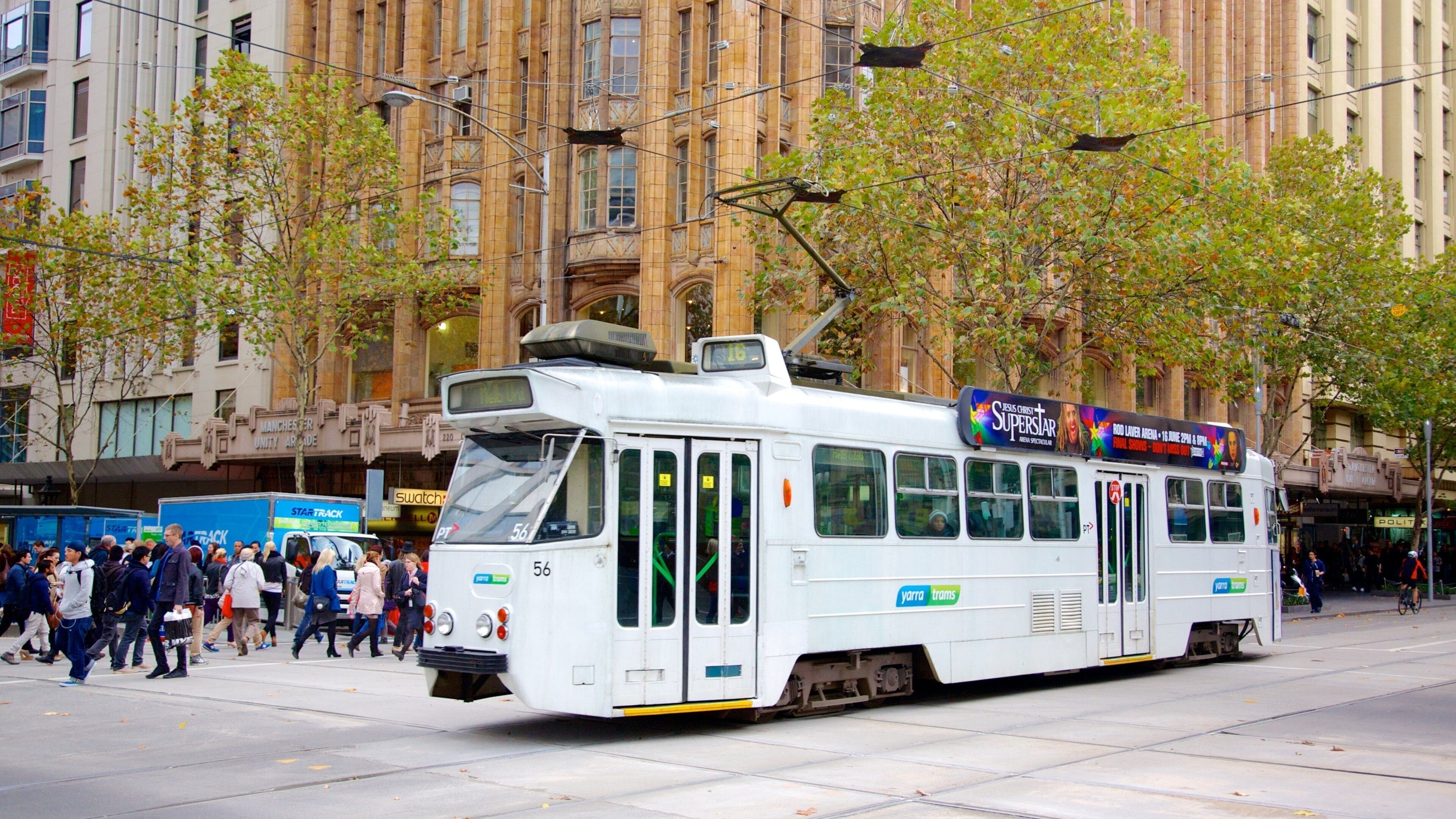 Un tramway circule dans une rue de la ville, avec des piétons et des bâtiments en arrière-plan.