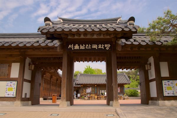 A traditional Korean gate with wooden pillars and tiled roof, leading to a courtyard with a pagoda.