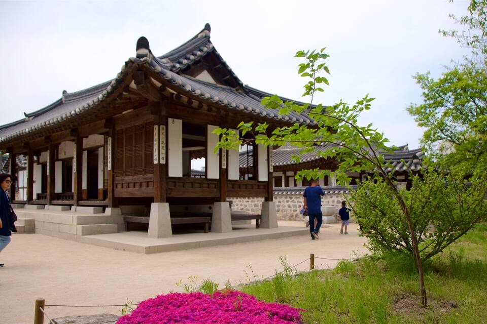 A traditional Korean building with a tiled roof and wooden beams, surrounded by greenery and flowers.