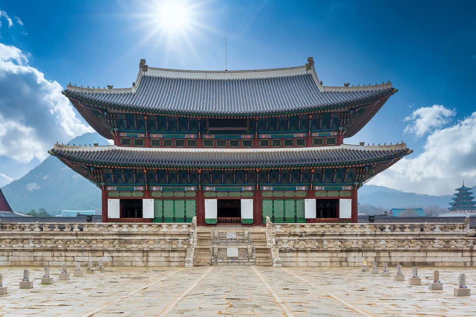 Un palacio coreano tradicional con un tejado escalonado, senderos de piedra y un telón de fondo montañoso.