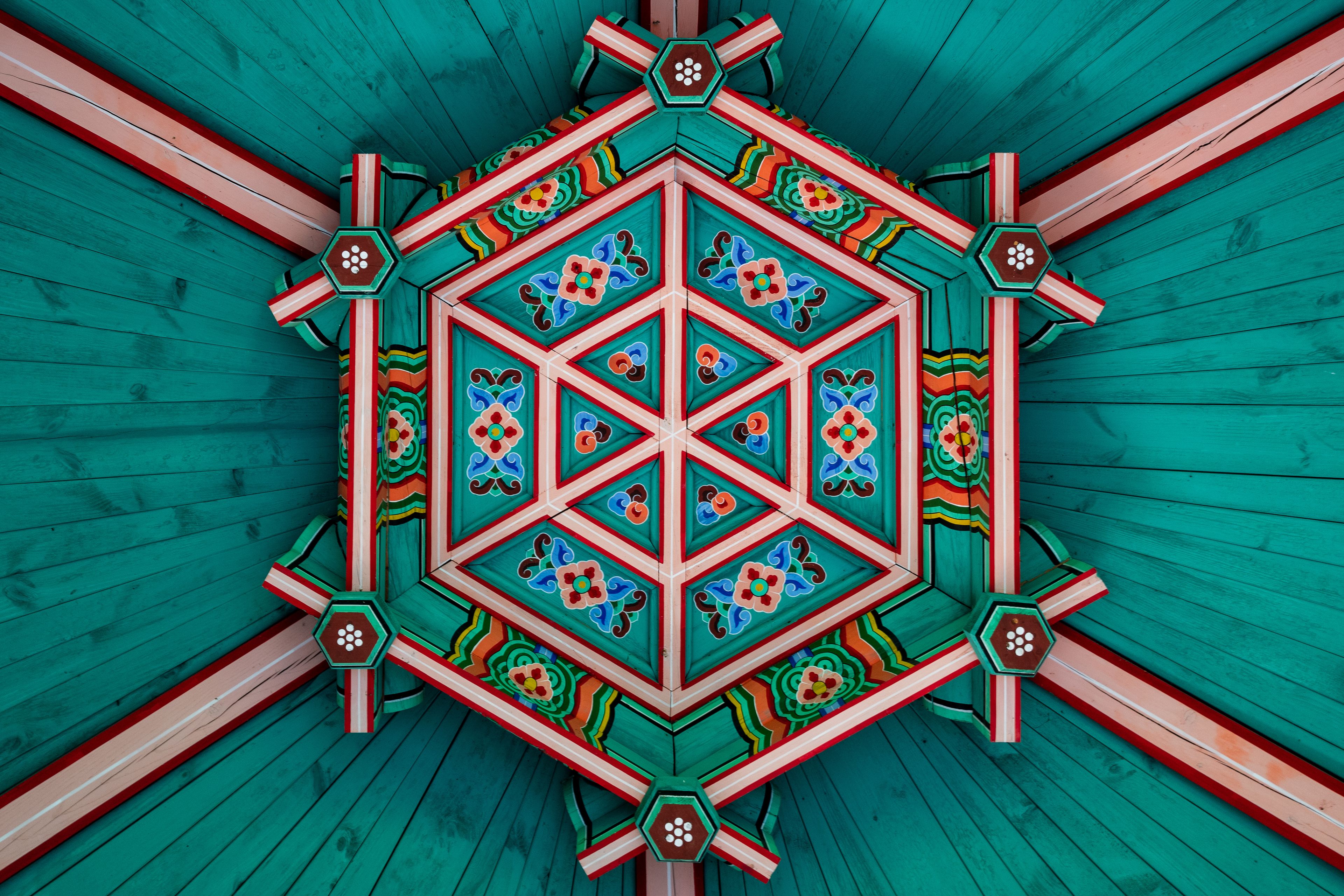 A geometric ceiling design with a central hexagonal pattern surrounded by a diamond shape, featuring floral motifs and a color scheme of teal, red, and green.