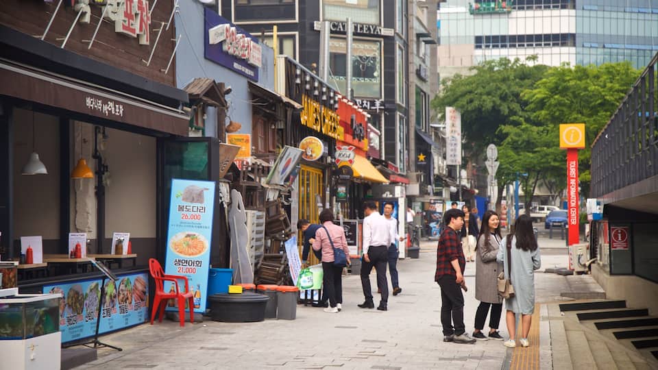 Una concurrida calle urbana con diversas tiendas, incluyendo un restaurante con un letrero llamativo.