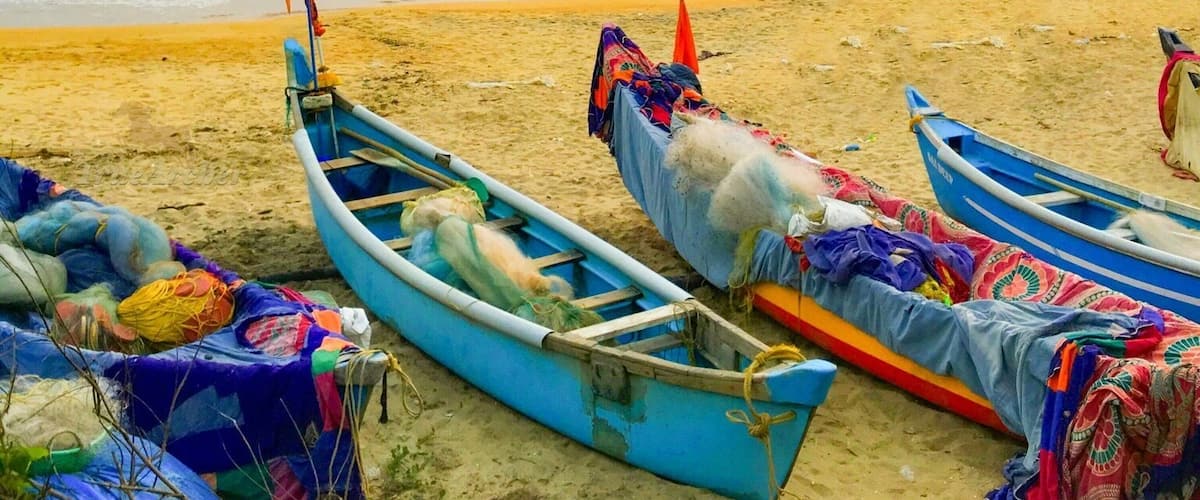 A beach with several small boats lined up on the sand, some covered with colorful fabric.