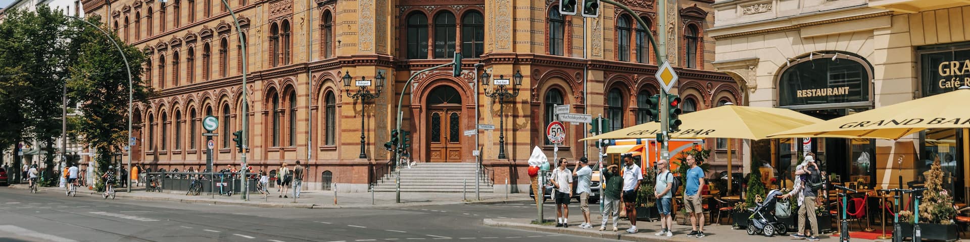 A historic building with ornate architecture, a prominent dome, and a street with pedestrians and cafes.