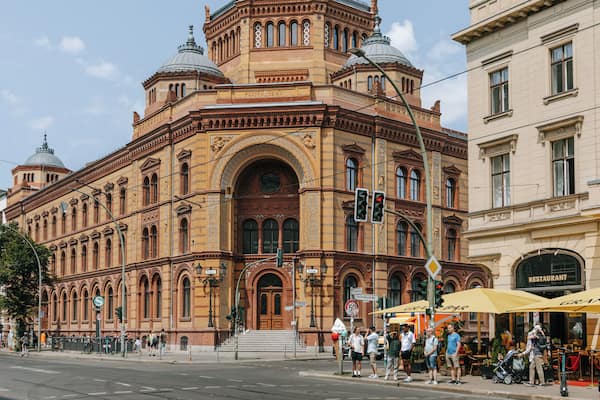 Ein historisches Gebäude mit aufwendiger Architektur, einer markanten Kuppel und einer Straße mit Fußgängern und Cafés.
