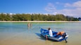 A clear beach with a blue boat anchored near the shore, a sandy beach, and a line of trees in the background.