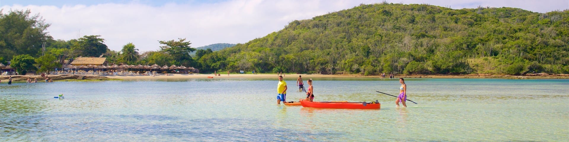 A tropical beach with clear waters, a small boat, and a lush green hill in the background.