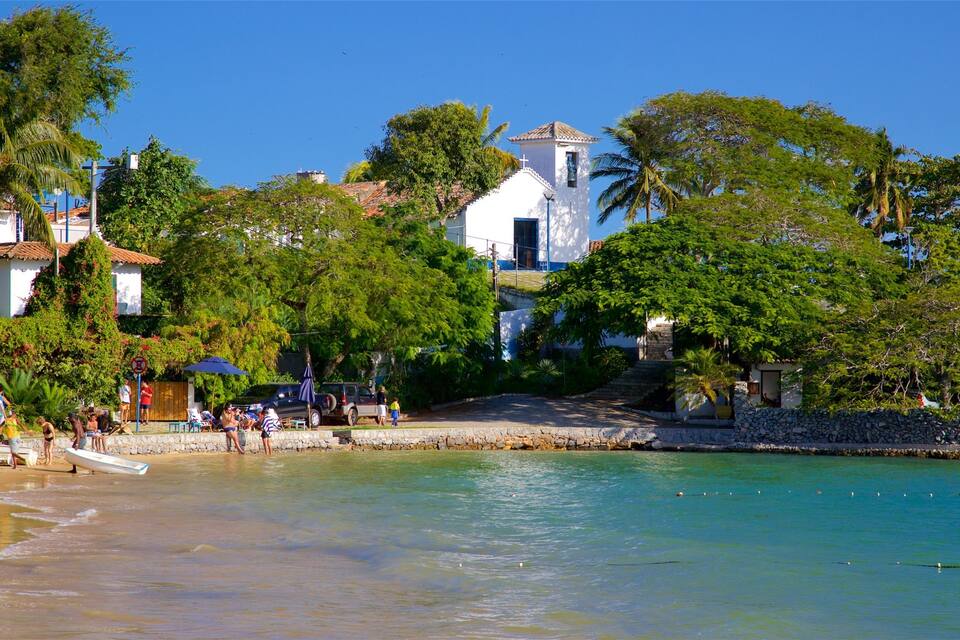 A beach with clear turquoise water, palm trees, and a white church with a bell tower.