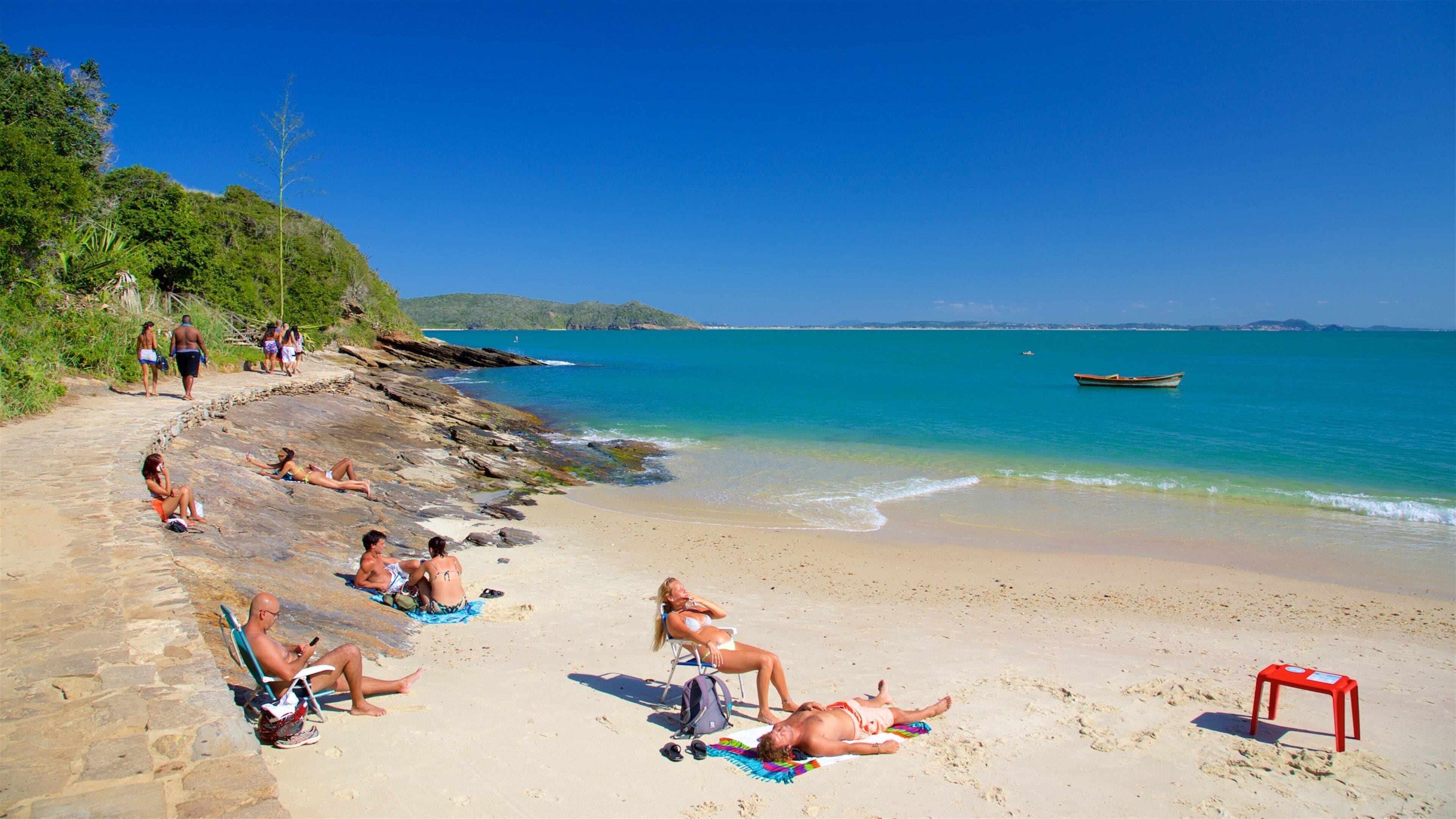 A sunny beach with people sunbathing and relaxing on the sand.