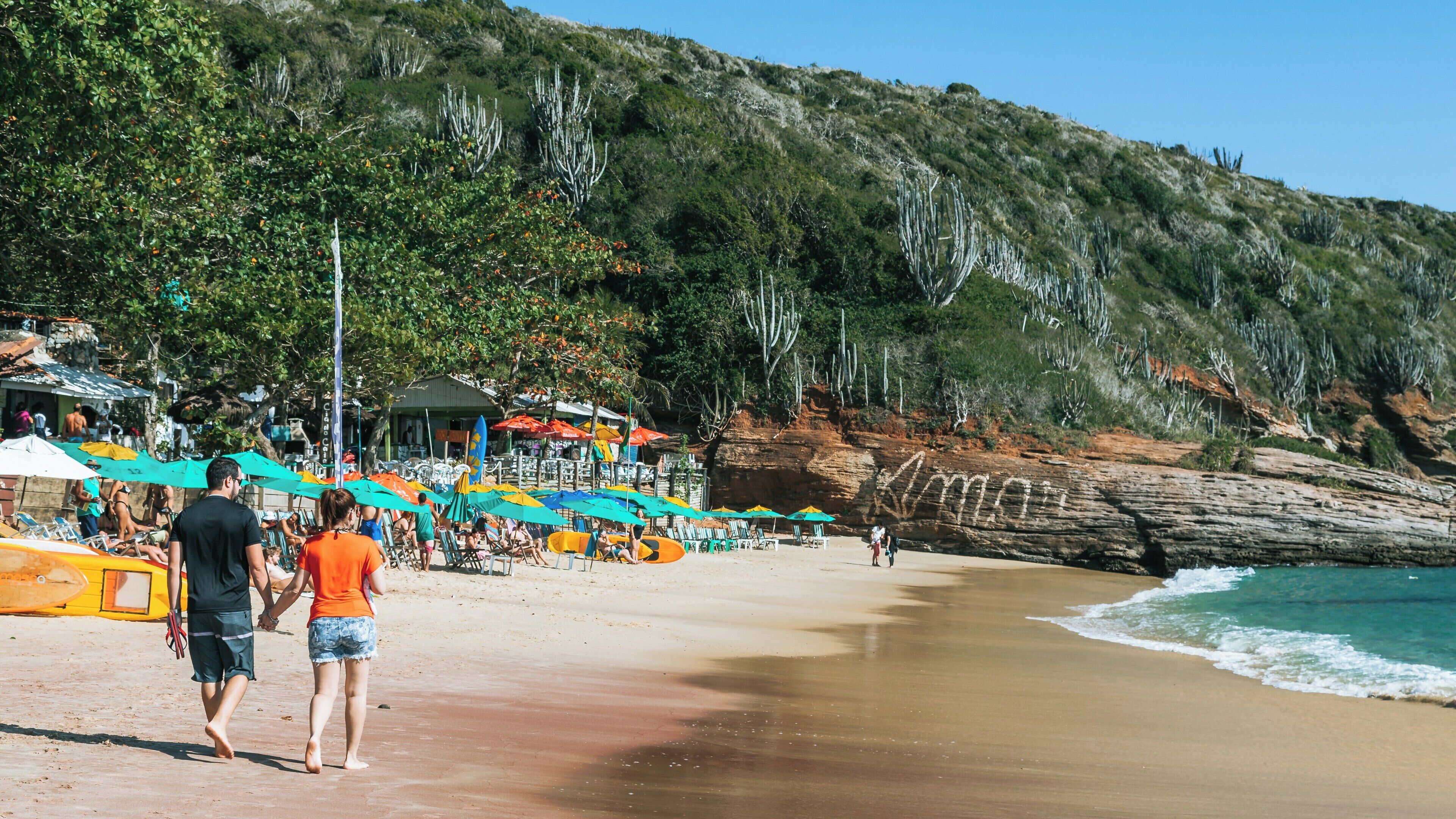 Strolling along João Fernandes Beach in Búzios, Rio de Janeiro on a sunny day filled with relaxed beachgoers and vibrant umbrellas