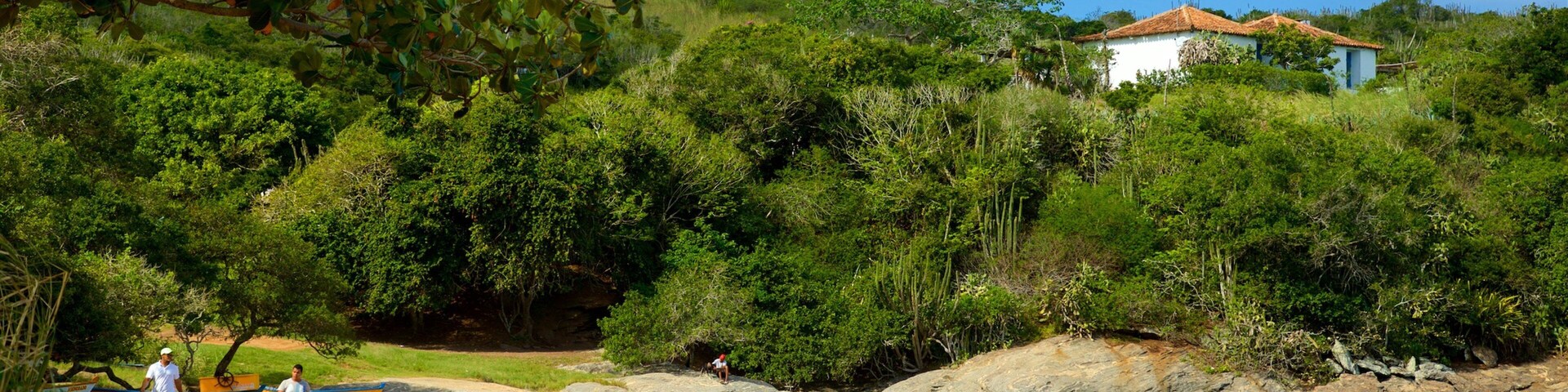 Une plage où des gens se détendent, un bateau et une maison située sur une colline.