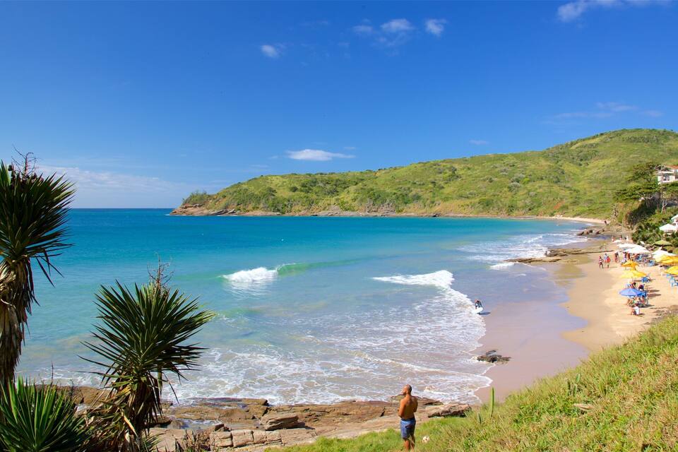 A beach with clear turquoise water, a sandy shore, and a hillside with greenery.