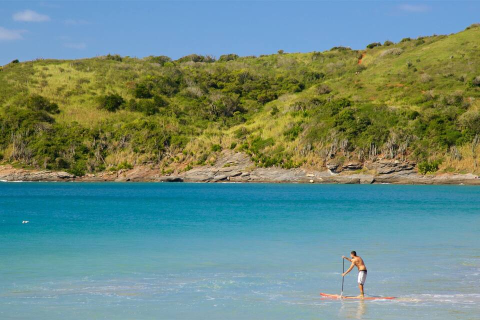 A person paddleboarding on a calm sea with a green hillside in the background.