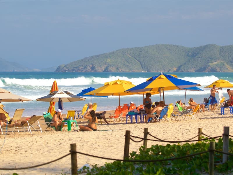 A beach with people relaxing under colorful umbrellas, beach chairs, and a wooden fence.