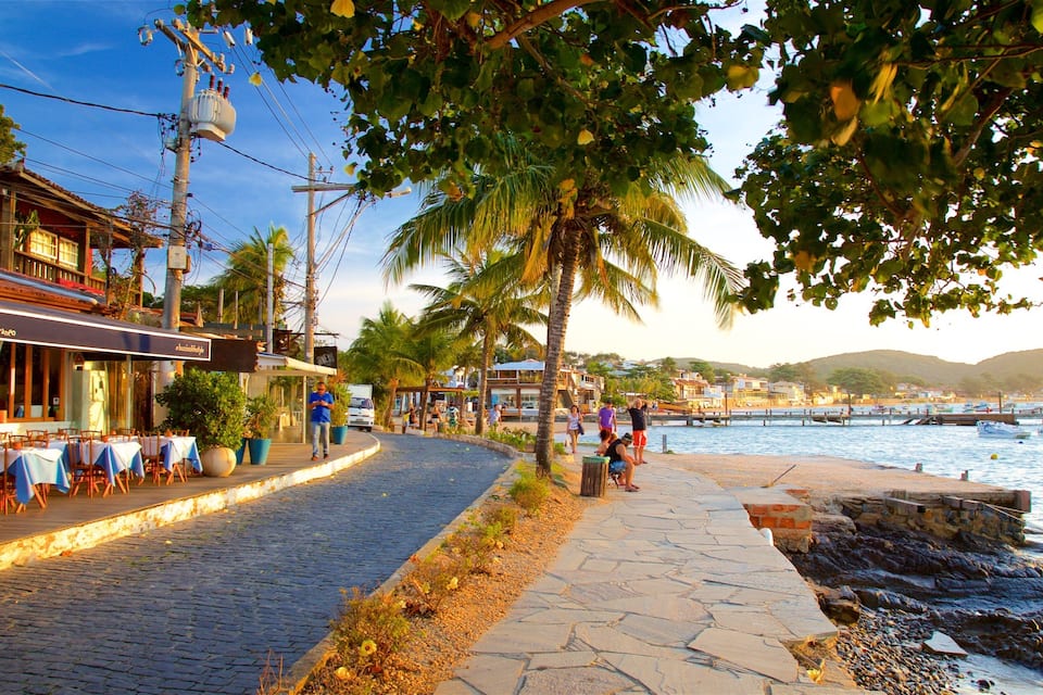 A cobblestone waterfront street with outdoor seating, palm trees, and a view of the sea.