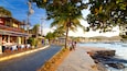 A cobblestone waterfront street with outdoor seating, palm trees, and a view of the sea.