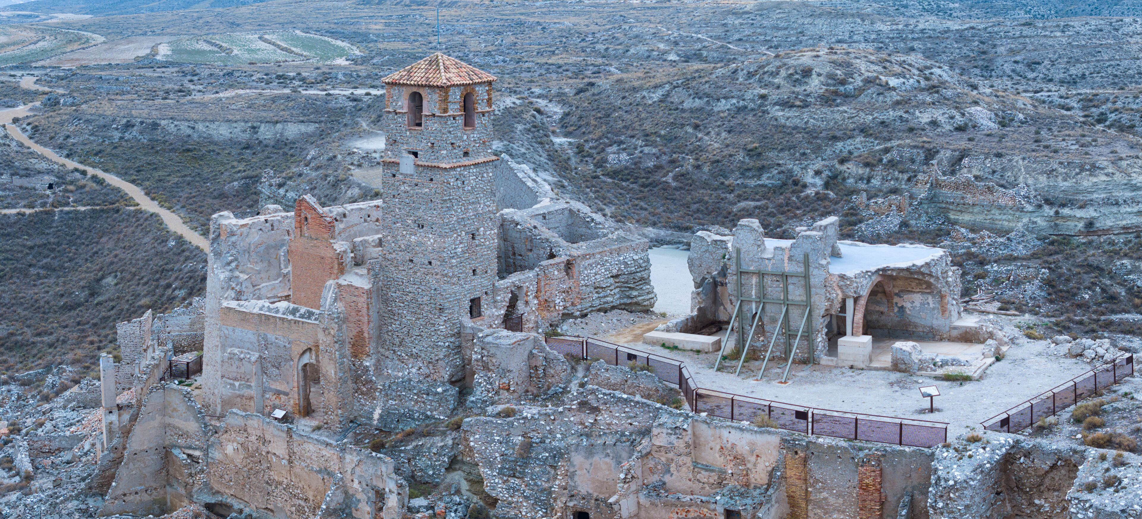 A historic stone fortress with a watchtower, surrounded by rugged terrain and a distant valley.