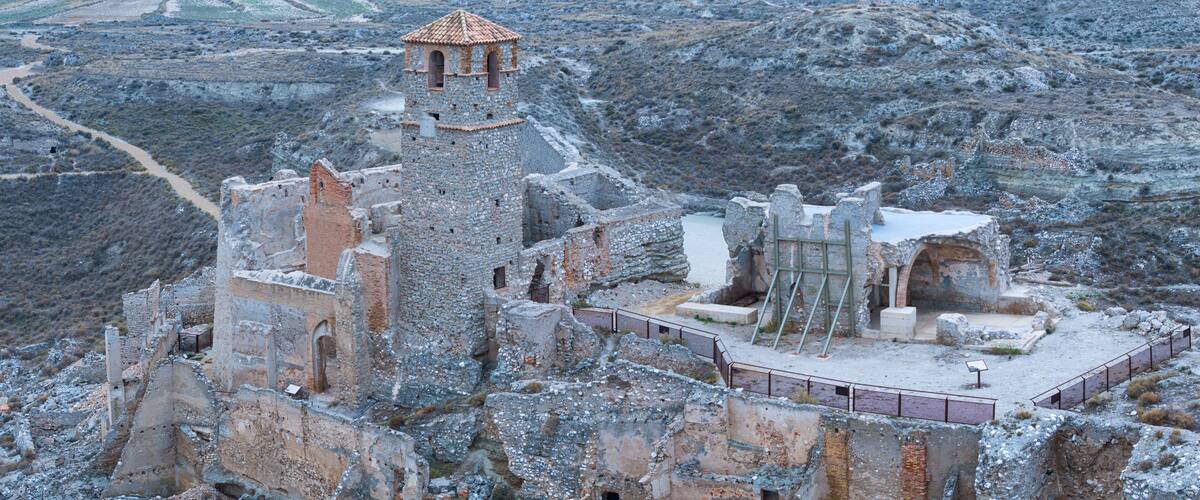 A historic stone fortress with a watchtower, surrounded by rugged terrain and a distant valley.