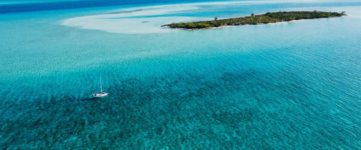 A clear turquoise sea with a small island and a sailboat.