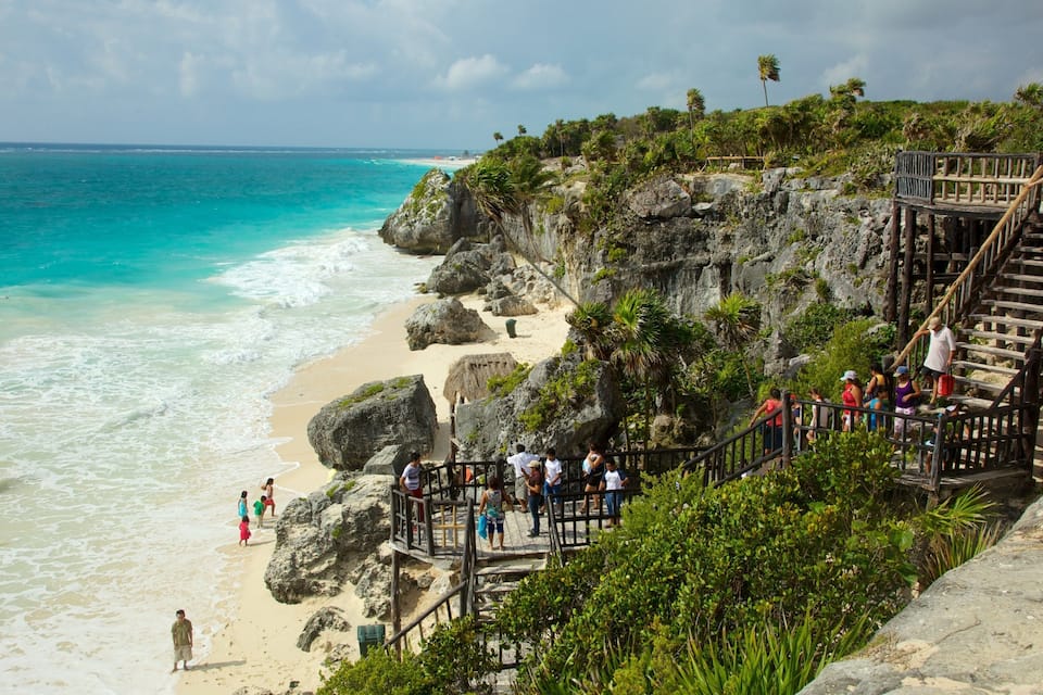A beach with a wooden staircase leading down to the shore, surrounded by rocks and palm trees.
