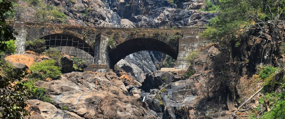 A waterfall cascading over rocks, a stone bridge, and lush greenery.