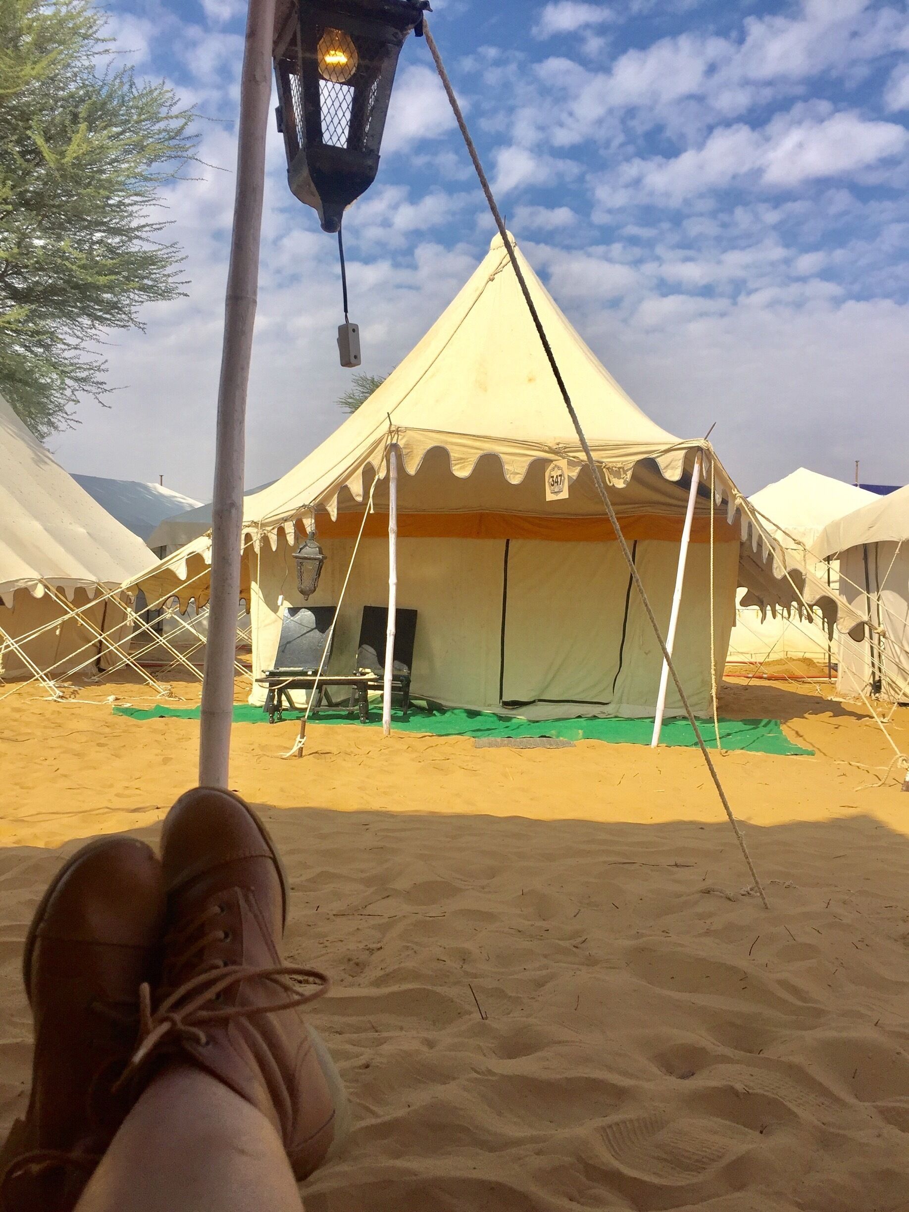 A desert campsite with tents, a hanging lantern, and a person's legs in a relaxed position.