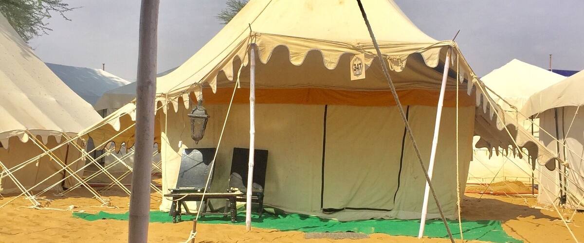 A desert campsite with tents, a hanging lantern, and a person's legs in a relaxed position.