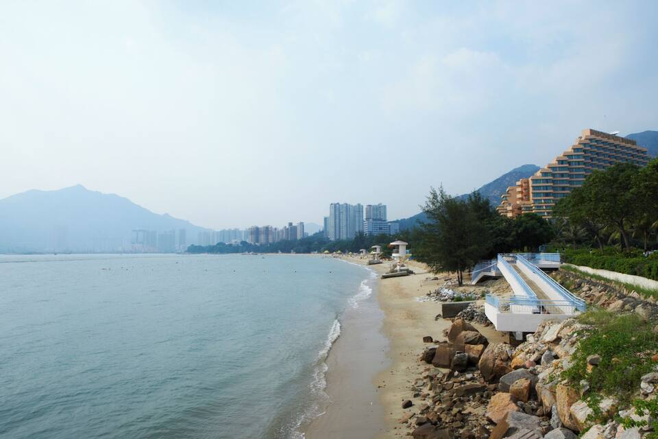 A beach with rocky shoreline, a lifeguard tower, and high-rise buildings in the background.