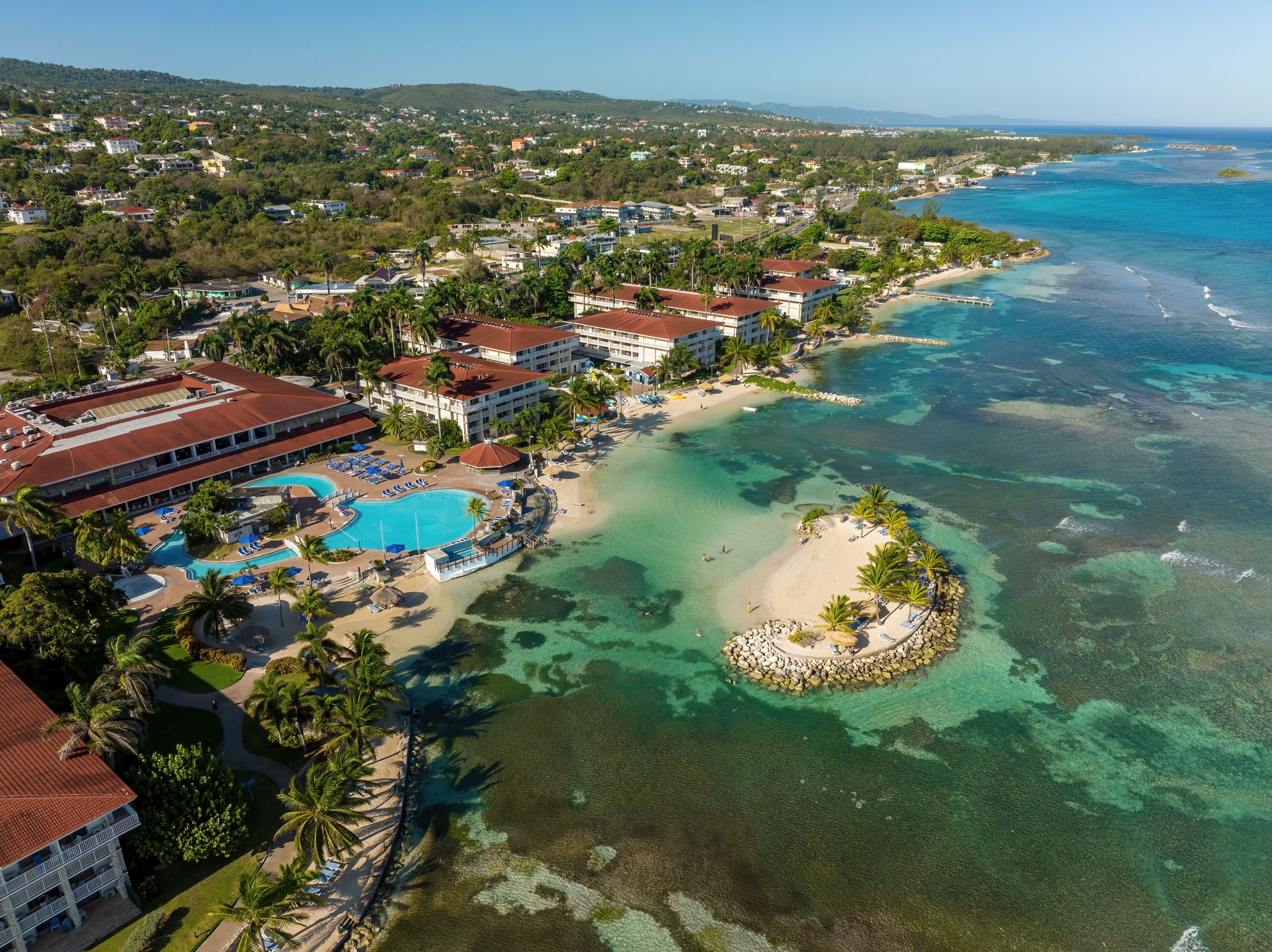A coastal resort with a swimming pool, beach, and clear turquoise waters.