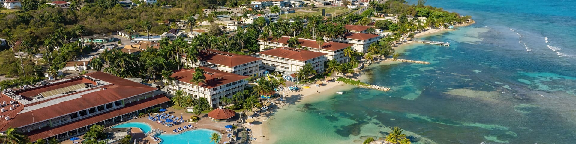 A coastal resort with a swimming pool, beach, and clear turquoise waters.
