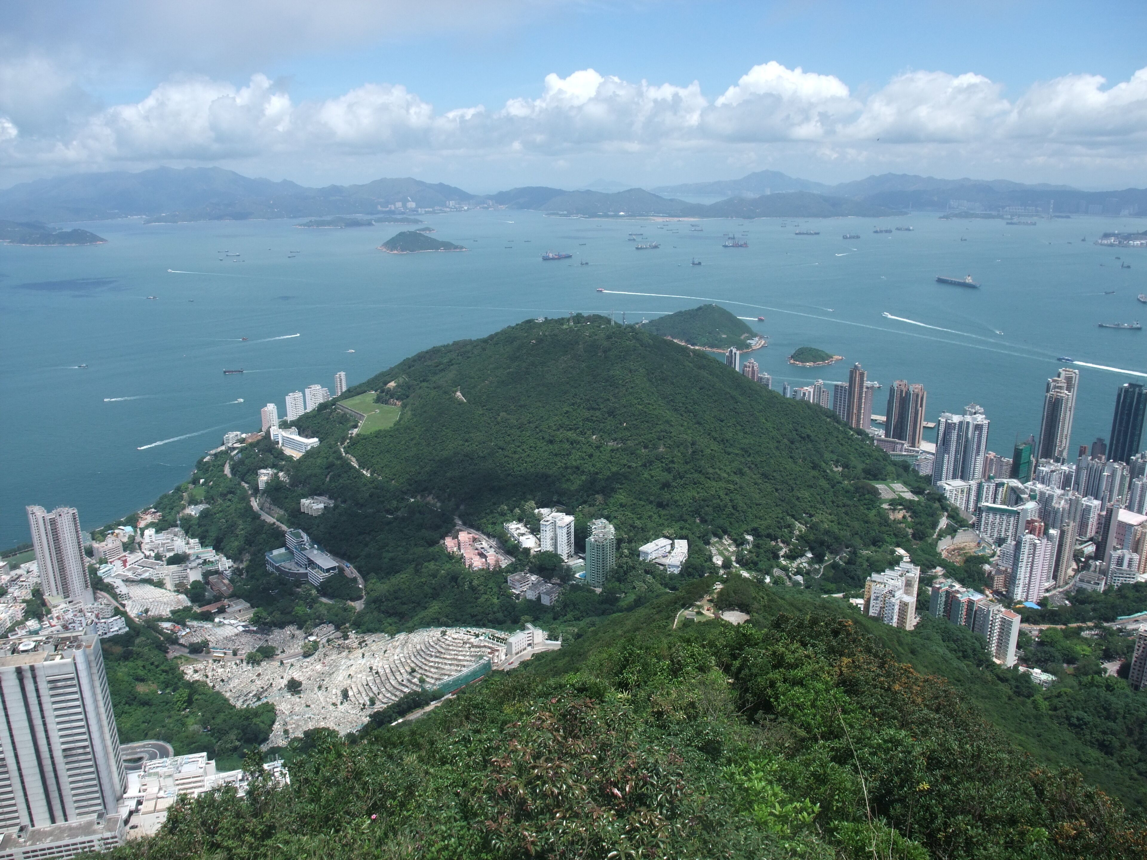 A coastal cityscape with a prominent hill, dense urban buildings, and a bay filled with boats.