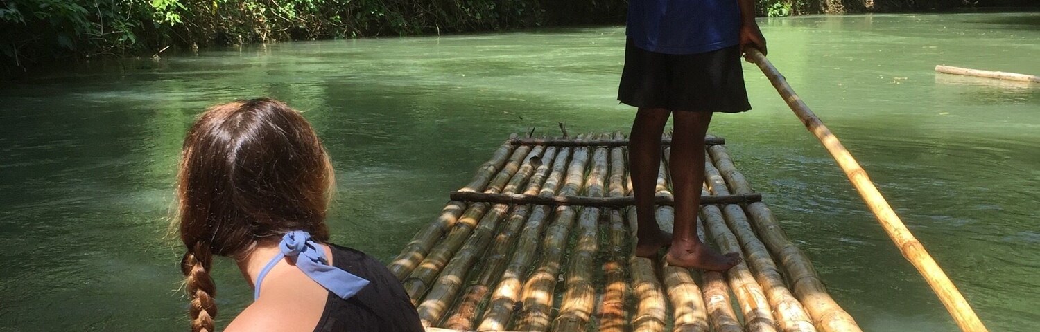 Una persona de pie en una balsa de bambú en un río rodeado de frondosa vegetación verde.