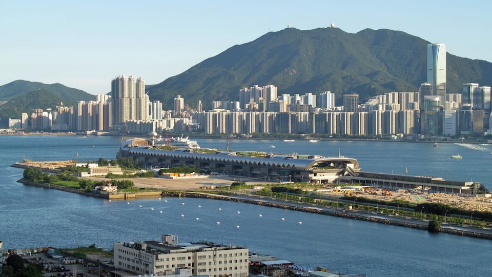 Un paysage urbain côtier avec de hauts immeubles, une marina et une montagne en arrière-plan.