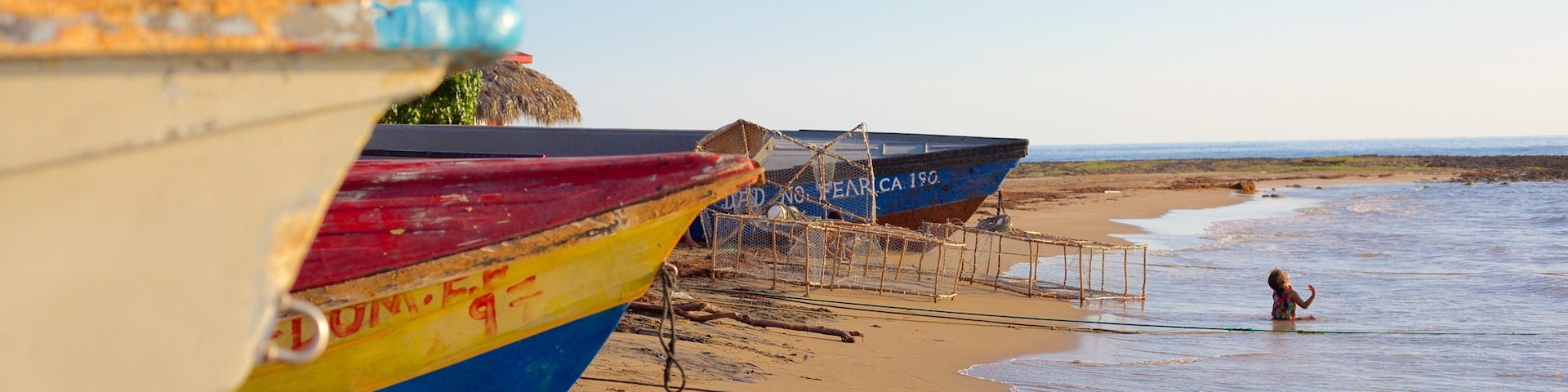 Colorful boats on a sandy beach with a child playing in the water.
