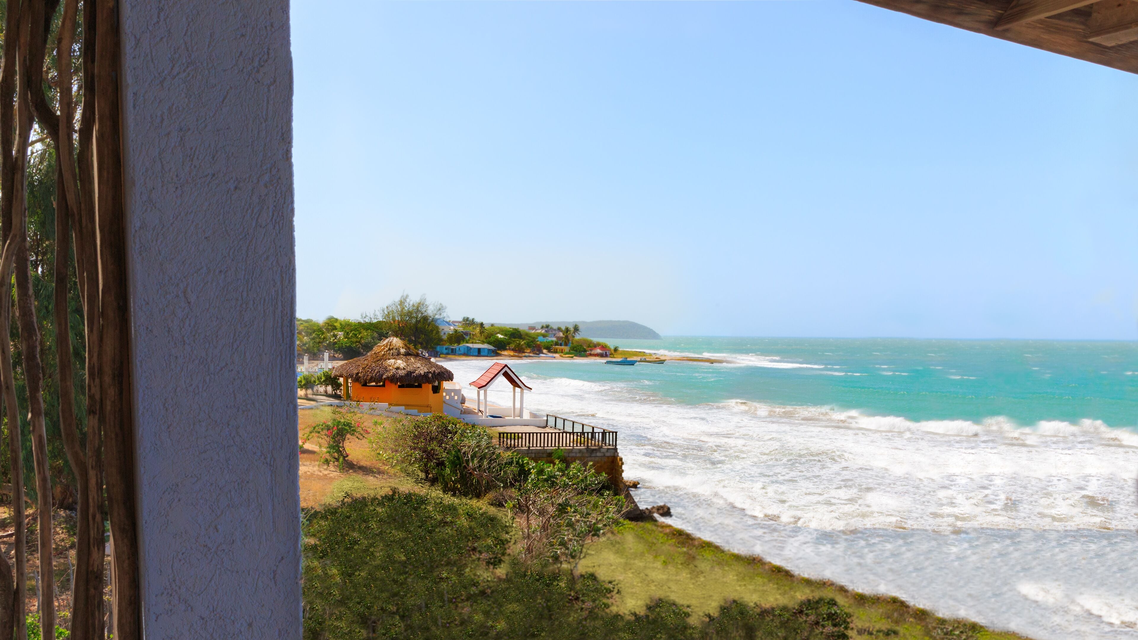 A beach with waves, a thatched-roof hut, and a wooden pier.