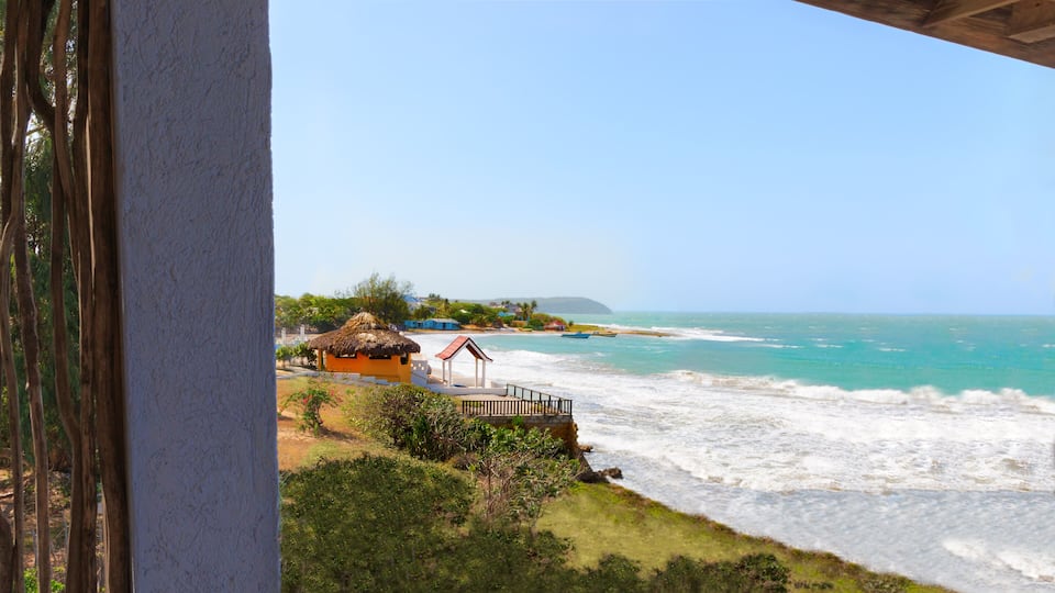 A beach with waves, a thatched-roof hut, and a wooden pier.