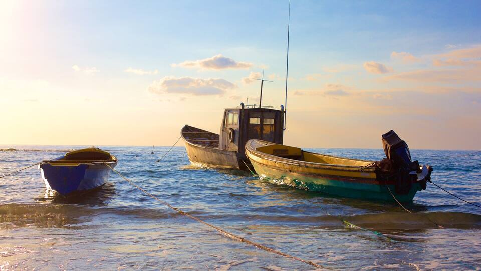 Two boats tied to a dock in a calm sea with a clear sky.