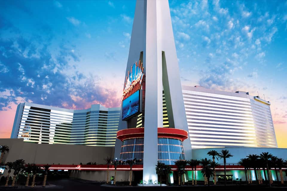 Un grande edificio moderno con una torre alta e slanciata e un cartello illuminato.