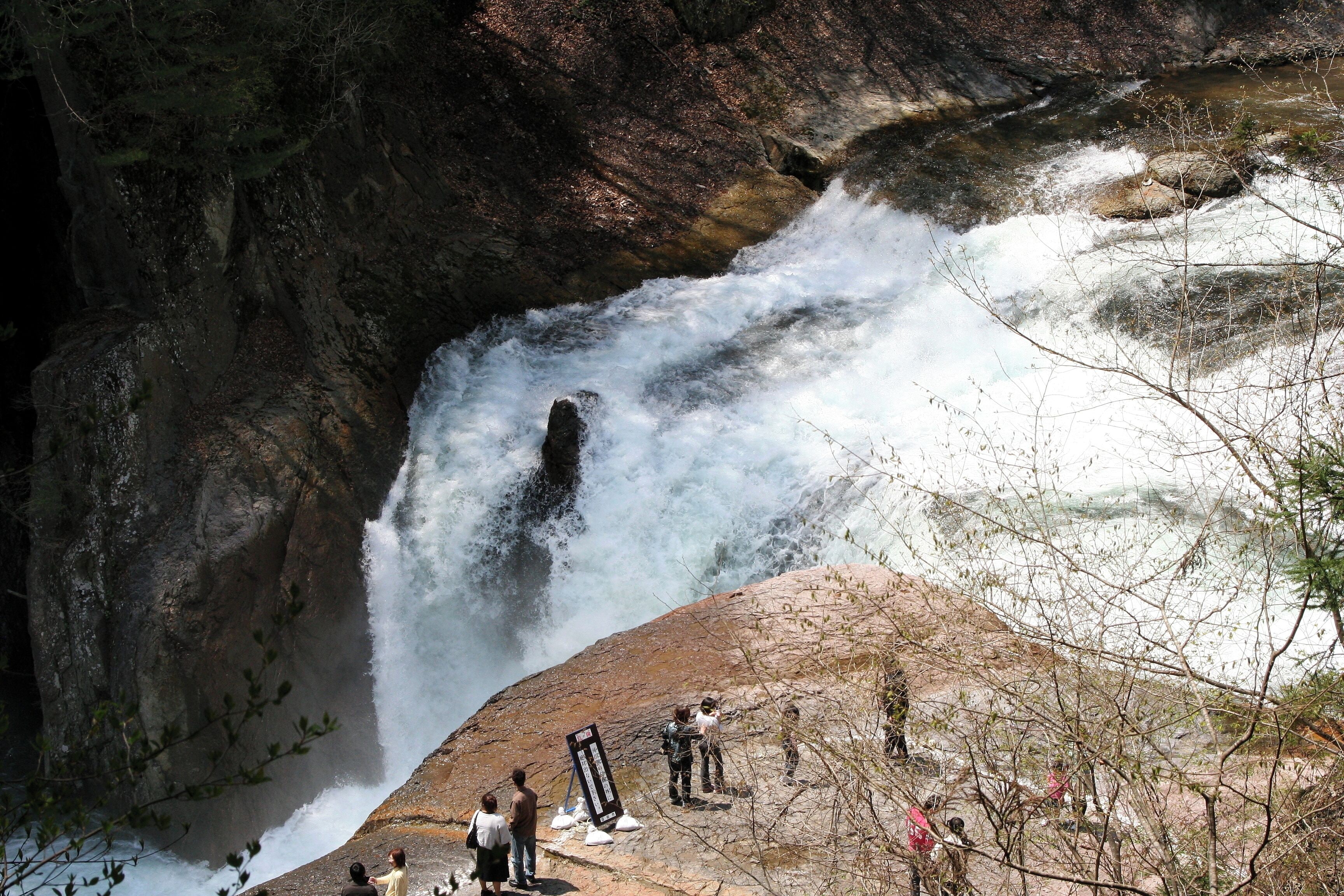 A waterfall cascading down a rocky cliff with people observing it.