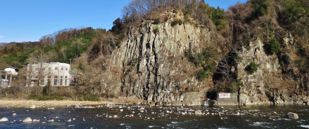 A river with rocks, a cliff with trees, and a building.